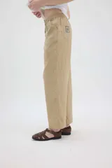 Pantalón de lino color beige, de silueta relajada, tiro medio-alto, cintura elastizada con cordón ajustable, bolsillos laterales y bolsillos traseros.