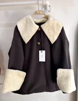 Sobre camisa marrón oscuro de paño de lana con cuello y puños de cuero de cordero color crema. Cierre frontal con botones dorados con el escudo de Uruguay.