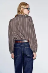 Camisa de manga larga con cuello subido, cierre frontal con botones y detalle de volantes en el pecho. Presenta un diseño a rayas verticales y puños elásticos.