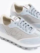 Zapatilla Mumi de cuero vacuno flor y descarne, color gris claro y celeste, con bordado "JCH" en el lateral. La base es de caucho para mayor liviandad y confort. Incluye cordón de algodón.