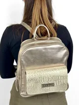 Mochila grande de cuero color dorado con bolsillo frontal con textura de piel de cocodrilo. Tiene asa de mano y correas ajustables para los hombros.