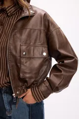 Campera corta de cuero sintético en color beige, con diseño de calce relajado, cierre frontal metálico, bolsillos con solapa en el frente y cordón ajustable en el ruedo.