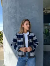 Chaqueta tejida en lana a rayas horizontales grises y azul marino, con cuello redondo, cierre frontal con botones dorados, bolsillos frontales con solapa y ribete en gris oscuro.