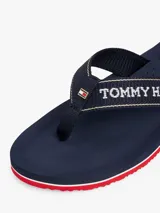 Ojotas de hombre color azul marino con tiras de textil trenzado que llevan el logo de Tommy Hilfiger en jacquard blanco. La suela es de EVA dentada con entresuela a contraste en blanco y rojo.
