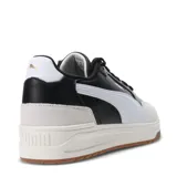 Championes Puma modelo Shuffle Downtown, de diseño retro urbano. Presentan una base blanca con detalles en negro, incluyendo la franja lateral característica de la marca, y refuerzos de gamuza en la puntera y el talón. Cuentan con suela de goma color caramelo y plantilla SoftFoam+ para mayor confort.