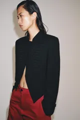 Blazer negro ZW Collection con cuello perkins, manga larga con vuelta en los puños y bajo asimétrico. Presenta detalles de alamares bordados en el frente.
