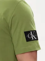 Remera verde oliva de algodón, corte clásico, cuello redondo y manga corta. Presenta una insignia con el monograma de Calvin Klein en la manga.