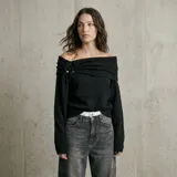 Buzo de tejido de punto color negro con diseño asimétrico y escote tipo hombros caídos. Presenta un detalle de aro metálico plateado en el frente que genera un drapeado artesanal y elegante.