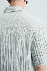 Camisa de manga corta con cuello solapa, confeccionada en tejido de mezcla de lyocell con textura de efecto arrugado y cierre frontal de botones.