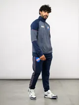 Buzo deportivo de medio cierre marca Umbro del Club Nacional de Football. Presenta un diseño en tonos azul y gris jaspeado, con cuello alto, mangas largas y detalles de costuras en contraste. Incluye el escudo del club y logo de la marca en el pecho.
