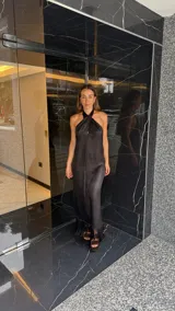 Vestido largo negro con escote halter cruzado y abertura frontal. El ruedo presenta un detalle de flecos.