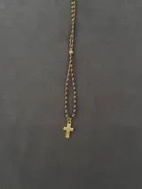 Collar con dije de cruz dorada y tira de tela trenzada combinada.