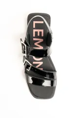 Sandalias planas de cuero negro charol con doble tira frontal ajustable mediante hebillas metálicas y tira en el talón.