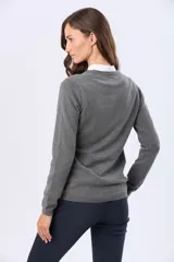 Buzo tejido en hilo de algodón color beige, con cuello redondo y manga larga. Presenta un corte clásico y un pequeño detalle metálico en la parte inferior izquierda.