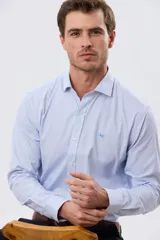 Camisa de vestir de manga larga con diseño de rayas finas celestes y blancas, cuello clásico y cierre frontal con botones. Incluye pequeño logo bordado en el pecho.