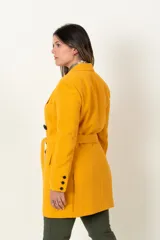 Chaqueta cruzada color mostaza con cierre de botones negros, bolsillos con tapa y detalle de botones en los puños.