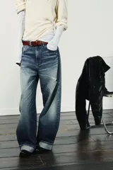 Jeans de mezclilla azul con lavado desgastado y rotos en la pierna derecha. Tienen tiro medio, corte ancho (baggy) y puños doblados en el bajo.