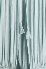 Vestido midi de tejido texturizado color verde menta, con escote redondo fruncido, espalda semiabierta con breteles finos y capa decorativa sobre los hombros. Cuenta con sección de punto smock en la cadera y falda con leve vuelo.