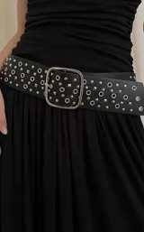 Cinto de cuero sintético negro con hebilla metálica cuadrada, decorado con tachas circulares y cuadradas en toda su superficie.