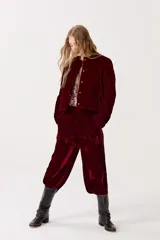 Pantalón de terciopelo color borgoña, de tiro alto, con cintura elástica en la espalda, cierre frontal, bolsillos laterales y piernas anchas.