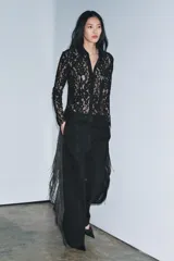 Camisa de manga larga confeccionada en encaje negro con patrón floral. Presenta cuello solapa de tejido liso negro y cierre frontal de botones. El bajo del ruedo y los puños tienen terminación de encaje festoneado.
