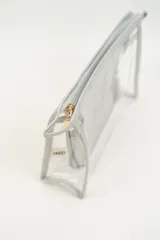 Neceser transparente con bordes y cierre en color beige claro, que incluye un neceser interior más pequeño de color plateado brillante.