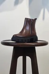 Bota de caña corta color marrón, con cierre lateral y suela track negra de goma con plataforma.