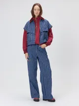 Campera de denim a rayas verticales con cuello de pana en color bordó. Presenta cierre frontal, mangas desmontables con cierre en los hombros, canesú en el pecho y bolsillos de parche cuadrados.