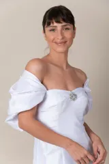 Vestido blanco de tafeta, strapless, con detalle de broche bordado en el escote. Presenta cinta trenzada en la espalda para ajustar y mangas caídas removibles. Vestido con cola.