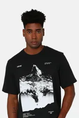 Remera negra de corte relajado con estampado gráfico frontal de una montaña y detalles de texto en blanco. Confeccionada en algodón, presenta cuello redondo y mangas cortas.