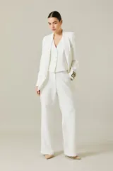 Saco tipo smoking de color blanco, con solapas satinadas y corte entallado. Presenta un diseño sofisticado con cierre frontal y detalles en los puños.