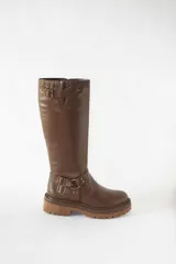 Bota de caña alta confeccionada en cuero color marrón, con suela track gruesa antideslizante. Presenta estribo decorativo con hebillas metálicas en el tobillo y detalle de ajuste con hebilla en la parte superior de la caña.