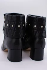 Botas cortas de cuero negro con taco cuadrado y punta fina. Presentan cuello caído capitoneado con apliques brillantes y cierre lateral con cremallera.