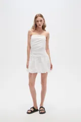 Vestido corto strapless de color blanco, con diseño drapeado en el torso y falda estilo globo con ruedo voluminoso.