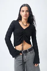 Top tejido negro con trama calada, escote en V, frunce central regulable y mangas acampanadas.