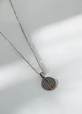 Collar de acero quirúrgico con dije circular calado que representa la flor de la vida, adornado con siete pequeñas piedras de colores que simbolizan los chakras.