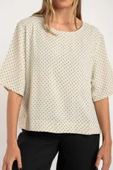Blusa cruda con estampado de lunares negros, de manga corta y cuello redondo.