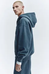 Campera con capucha de corte oversized, confeccionada en tejido de mezcla de algodón con interior suave. Presenta cierre frontal, hombros caídos, cordón ajustable en la capucha y bolsillos tipo canguro. Puños y bajo acanalados.