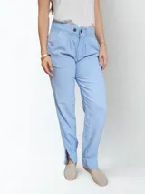 Pantalón celeste de lino con pinzas en la cintura, bolsillos laterales y corte a la altura del tobillo con aberturas laterales.
