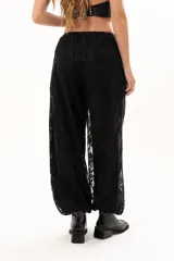 Pantalón de encaje negro con diseño floral, corte holgado y cintura elástica con cordón ajustable. Cuenta con bolsillos laterales.