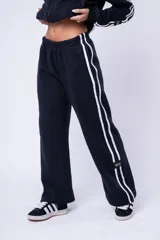 Pantalón de jogging color marrón, de corte recto y holgado, con cintura elástica y doble franja lateral blanca. Presenta una etiqueta pequeña con la marca en la parte inferior de la pierna.