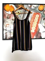 Vestido corto blanco con rayas verticales en azul, amarillo y marrón. Tiene escote redondo, breteles anchos y corte holgado.