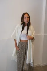 Ruana de tejido de punto color blanco, con textura tipo panal y terminaciones con flecos en el ruedo.