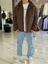 Campera puffer impermeable color beige con capucha desmontable con cordones negros, cierre frontal con cremallera y solapa con botones a presión.
