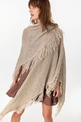 Ruana de punto color beige con diseño abierto y flecos en los bordes.