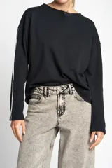 Sweater negro de calce oversize, confeccionado en algodón peinado con textura sutil. Presenta cuello redondo y una línea vertical blanca decorativa a lo largo de las mangas largas.