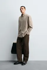 Camisa de algodón de manga larga, cuello abotonado y cierre frontal de botonadura. Presenta un patrón de cuadros pequeños en tonos beige, marrón y blanco.