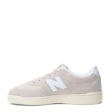 Championes urbanos New Balance modelo Court, color gris claro con detalles en blanco. Confeccionados en una combinación de gamuza y malla, presentan el logo 'N' característico en los laterales y una suela de goma en tono crema.
