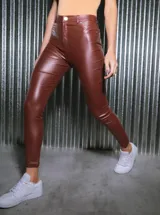 Pantalón de tiro alto confeccionado en bengalina engomada con acabado brillante. Presenta un diseño ajustado tipo chupín con cierre frontal, botones y remaches metálicos.