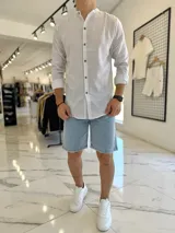 Camisa blanca con finas rayas azules, cuello mao y cierre frontal con botones marrones de efecto madera, de manga larga.